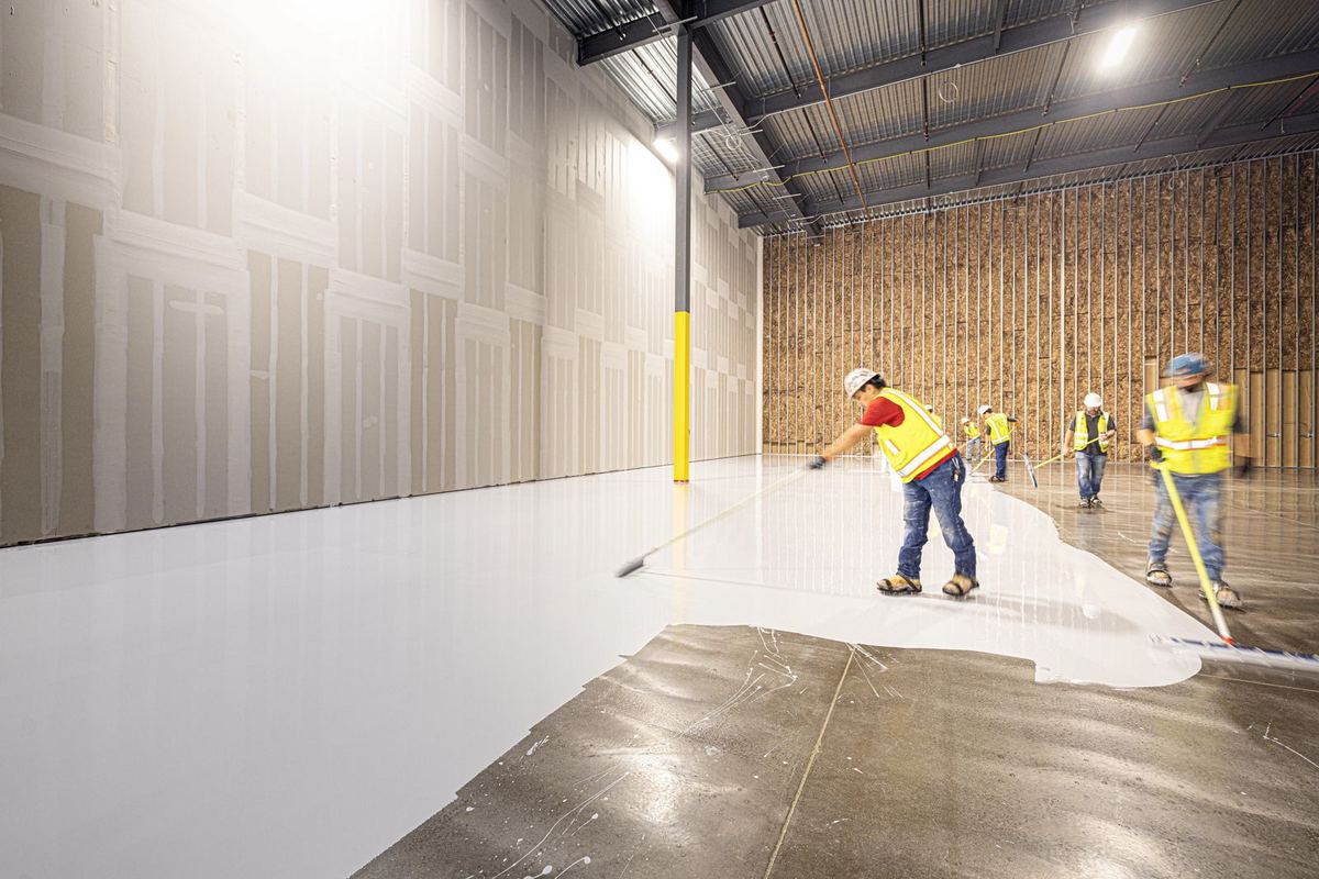 Crew applying a seamless white coating across a warehouse floor